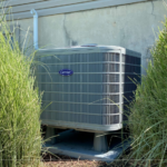 Carrier air conditioner installed in front of a beige house between two bushes