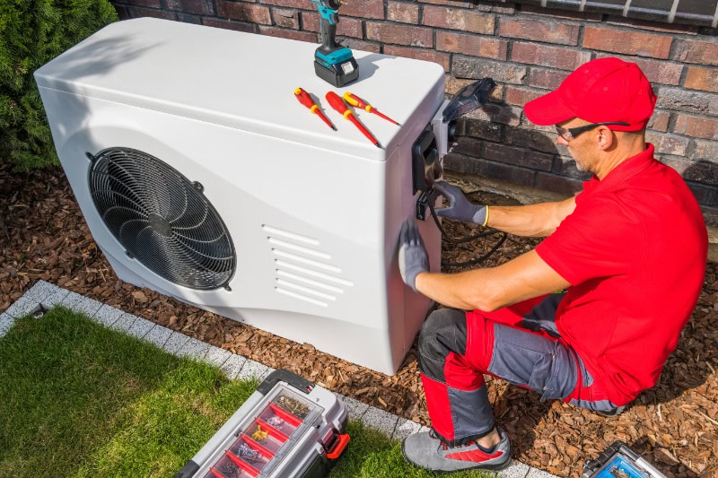 4 Factors to Consider When Buying a Heat Pump. Professional HVAC Technician Repairing Modern Heat Pump Unit.