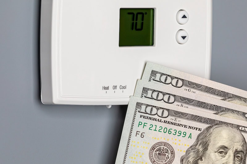 Wall thermostat with three, hundred dollar bills in front.